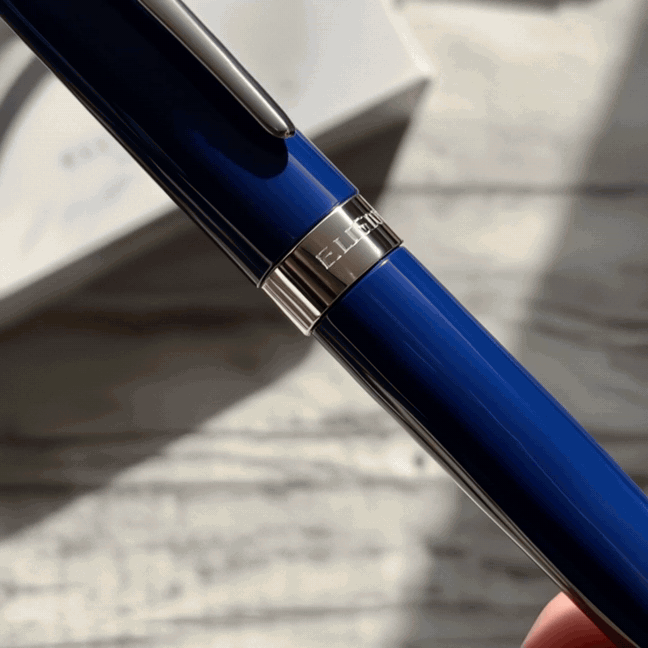 Blue Nautilus fountain pen with silver trim being uncapped and used to write